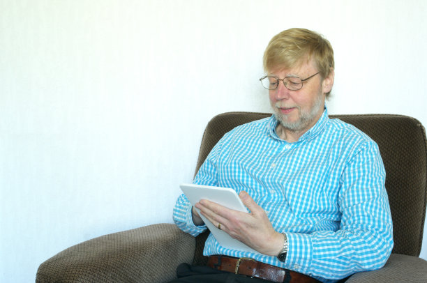 蓄着胡子的中年男子坐在扶手椅上，放松地用着平板电脑图片下载