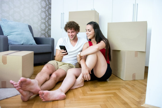 一对年轻夫妇在他们的新家使用智能手机，周围都是纸箱图片下载