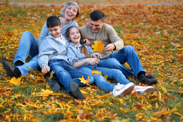 阖家欢乐，秋天城市公园。孩子们和家长们摆姿势、微笑、玩耍、玩得开心。亮黄色的树和树叶图片下载