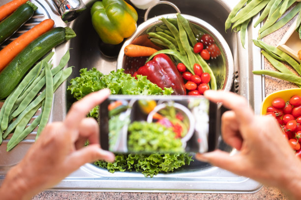 屋子里的女人在装满新鲜蔬菜的水槽前拍了张照片。绿色，红色和橙色是美丽的颜色图片下载