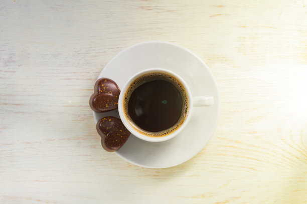 木桌上放着两颗心形巧克力和一杯咖啡。情人节庆祝概念。俯视图图片下载