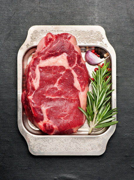 生牛排肋眼与迷迭香和大蒜在金属托盘，俯视图图片下载