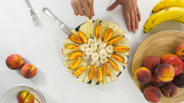 盘子里的苹果、香蕉和桃子片。女人手，白底俯视图。水果沙拉，水果拼盘，甜点图片下载