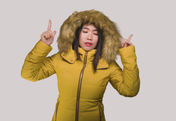 冬季时尚孤立的年轻美丽和快乐的亚洲中国女人的肖像在温暖的黄色羽毛夹克毛皮兜愉快和顽皮的微笑手势与甜蜜的脸表情图片下载