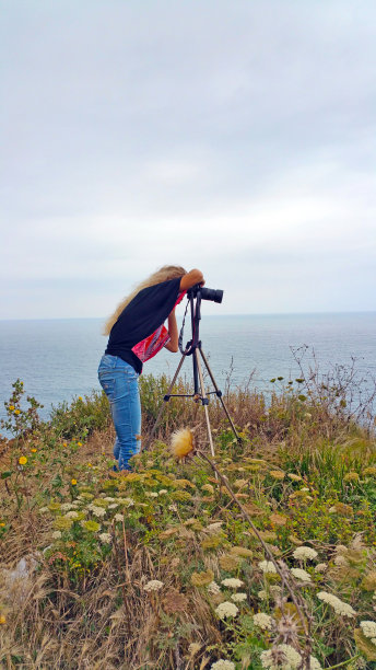金发女孩带着三脚架的相机从悬崖边拍摄大海图片下载
