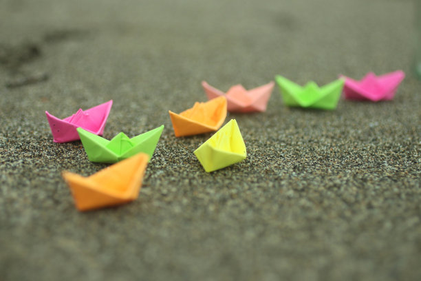 以海沙为背景的彩色纸船。图片下载