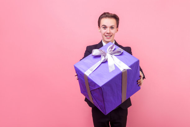 把它!正面的肖像，慷慨的男人在西装举着礼盒和微笑。工作室拍摄孤立的粉红色背景图片下载