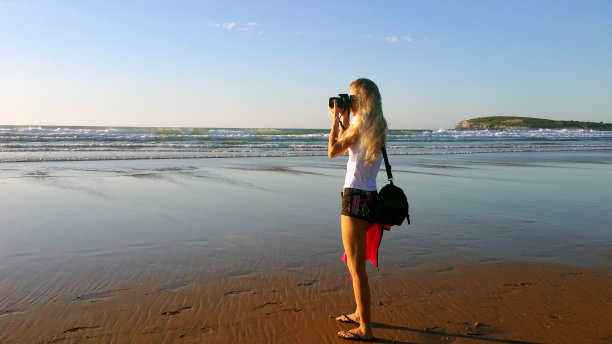 金发女孩拿着相机在海滩上拍照图片下载