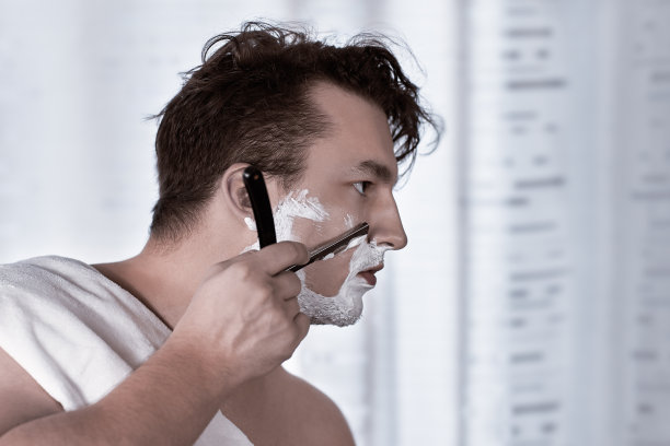 年轻英俊的白人男子手腕上戴着电子表用直剃须刀刮胡子，复古风格的老发型。图片下载