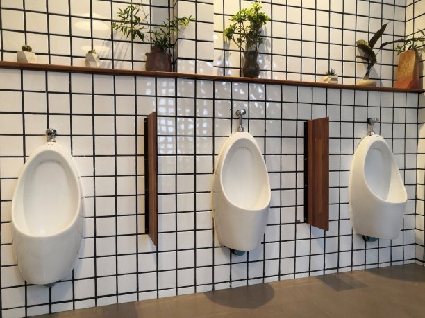男性小便池的模式在背景，陶瓷小便池在男性公共厕所排成一排。尿感染。男厕所。图片下载