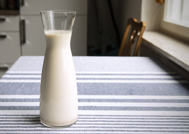 新鲜的自制燕麦牛奶在玻璃瓶立在厨房的桌子上。舒适的室内氛围，简单、朴实的健康植物奶。副本的空间。图片下载
