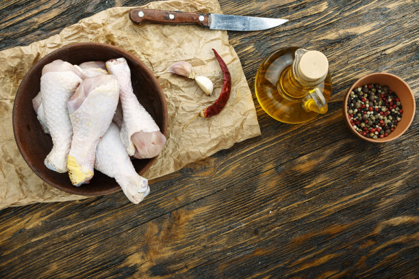 生鸡腿放在桌上的盘子里，旁边放着不同的香料。图片下载
