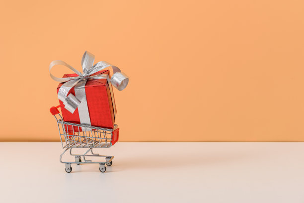 许多礼盒与红色丝带蝴蝶结和购物车或手推车在白色的桌子和柔和的橙色背景图片下载