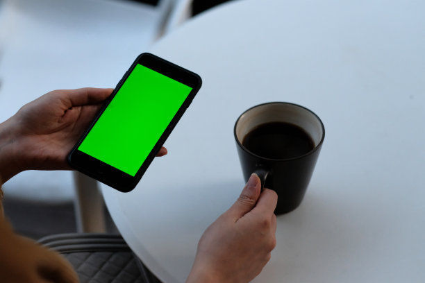 一个女人在咖啡馆拿着绿屏智能手机。图片下载