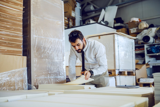 勤劳的蓄着胡子的白种图形工程师站在仓库里清点表格。图片下载