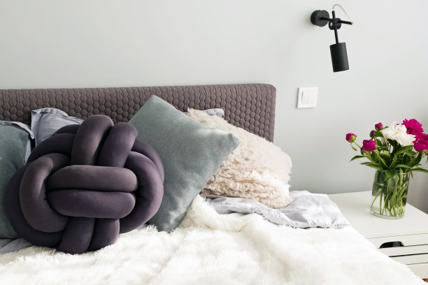 床上有很多装饰枕头，床头柜上放着牡丹。图片下载