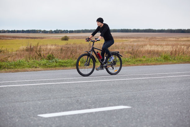 水平镜头的摩托车手穿着黑色的赛道服骑在有标记的柏油路上，运动的男性享受公路自行车，覆盖指定的距离，试图成为第一。运动和爱好的概念。图片下载