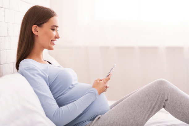 在家坐在床上使用智能手机的孕妇图片下载