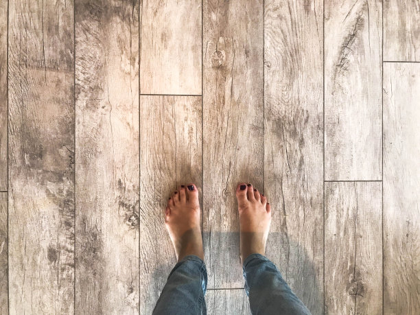 一个光着脚、修着红色指甲的女人正站在由厚木板铺成的新强化地板上。概念:乔迁，公寓装修，铺设层压板图片下载