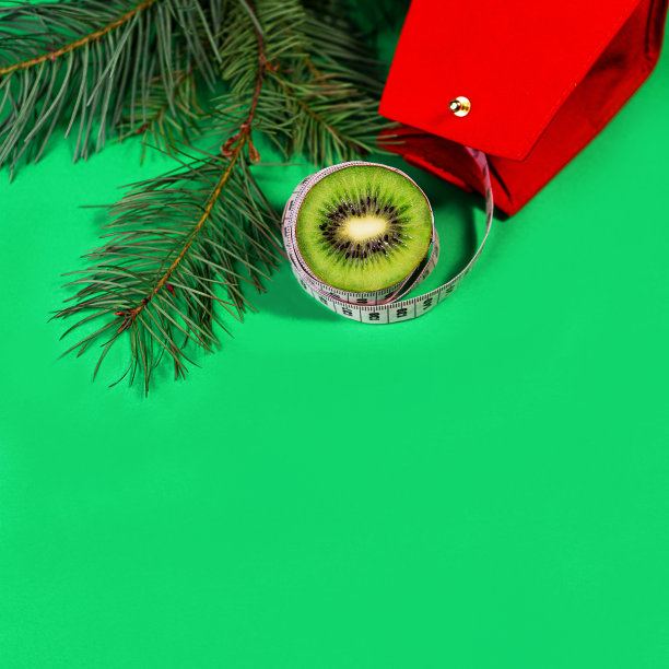 概念圣诞假期饮食和健康的生活方式-猕猴桃和卷尺与红色礼品袋和绿色冷杉树枝在时尚的绿蓝色背景。图片下载
