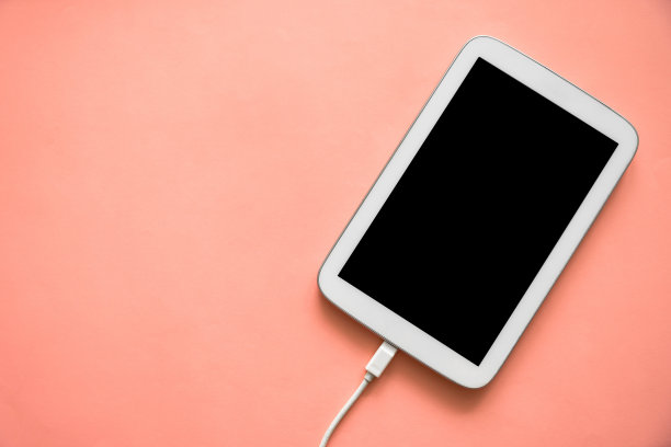 俯视图白色平板与黑色屏幕和充电电缆在粉红色纸颜色的背景。图片下载