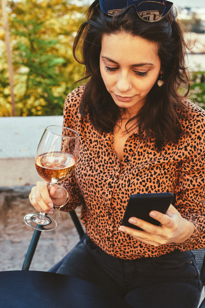 漂亮女人在户外用手机喝酒的照片。图片下载