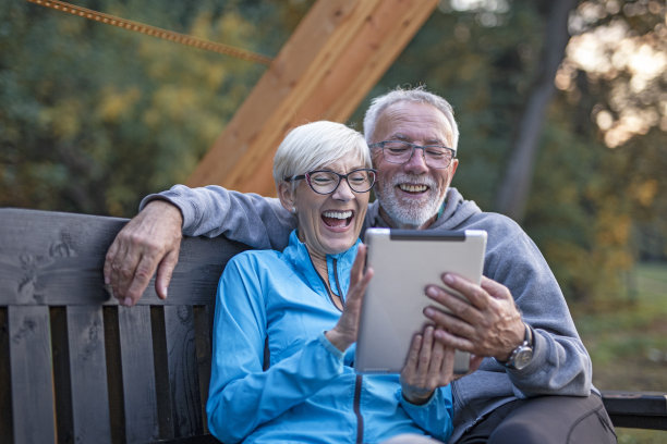 一对成熟的夫妇坐在长凳上，看着平板电脑，玩得很开心图片下载