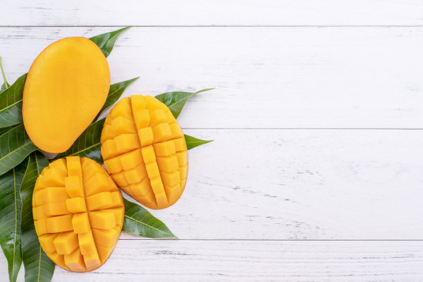 漂亮的切碎的成熟芒果与绿色的叶子在明亮的白色木质背景，俯视图，平铺，复制空间。热带水果设计理念。图片下载