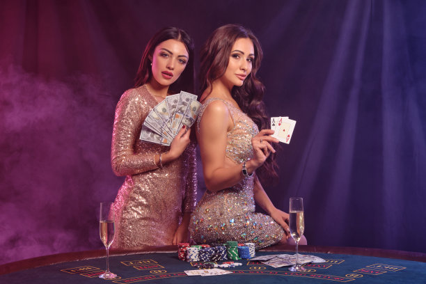 两个女人展示牌和钱，在赌场的桌子上摆姿势。黑色，烟雾背景与彩色的背光。赌博、打扑克。特写镜头图片下载