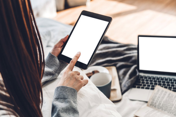 在家里的床上，一个女人正在放松，用着带有白色空白屏幕的平板电脑。女性查看社交应用程序和工作…交流和技术概念图片下载