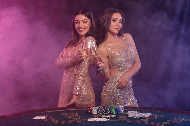两个女人喝着香槟，在赌场的赌桌前摆姿势。黑色，烟雾背景，彩色的背光。赌博、打扑克。特写镜头图片下载
