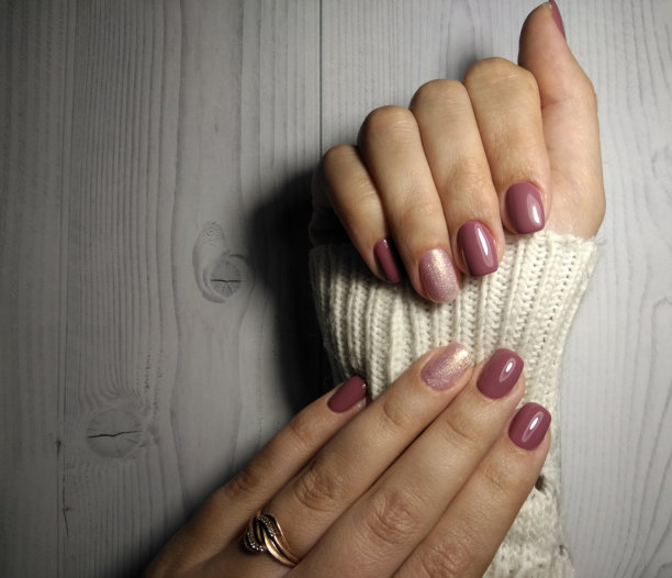 女士穿毛衣时，涂上浅暗红色的啫喱。柔和的深粉色涂层，有光泽的设计。用粉色漆装饰指甲。从上往下看。图片下载