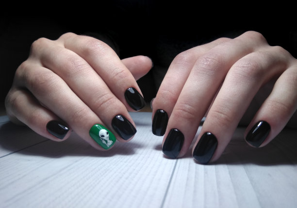 黑色光滑的指甲油在女性把手与白色外星人设计在绿色背景。配着外星人照片的时髦美甲。在木桌上做美甲。图片下载