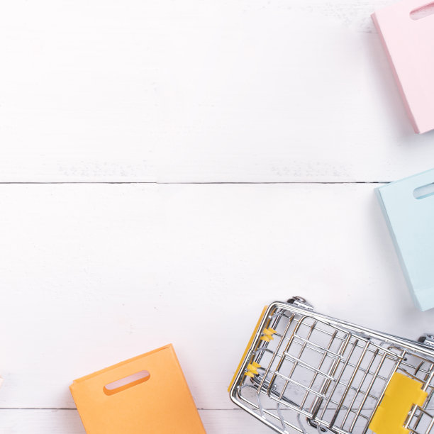 抽象的设计元素，年度销售，购物季节的概念，小手推车与彩色纸袋在白色木制桌子的背景。图片下载