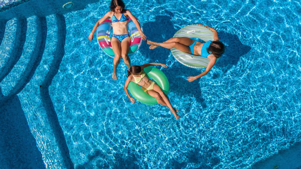 家庭在游泳池空中无人机从上面看，快乐的母亲和孩子游泳在充气圈甜甜圈和有乐趣的家庭度假，热带度假度假胜地图片下载