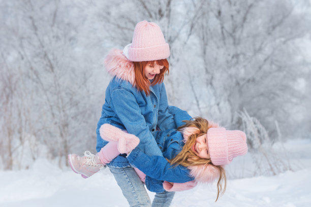 在冬天的树林里，年轻女子坐在雪地里，小女孩站在她旁边图片下载