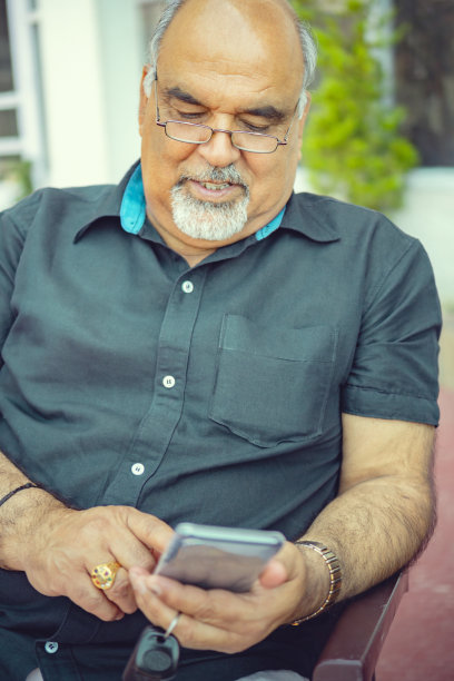 戴眼镜的退休老人在用智能手机。图片下载