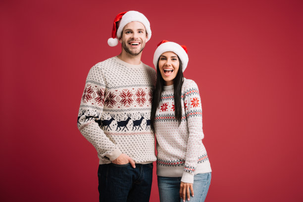 一对美丽兴奋的情侣戴着圣诞老人的帽子和毛衣在红色的孤立摆姿势图片下载