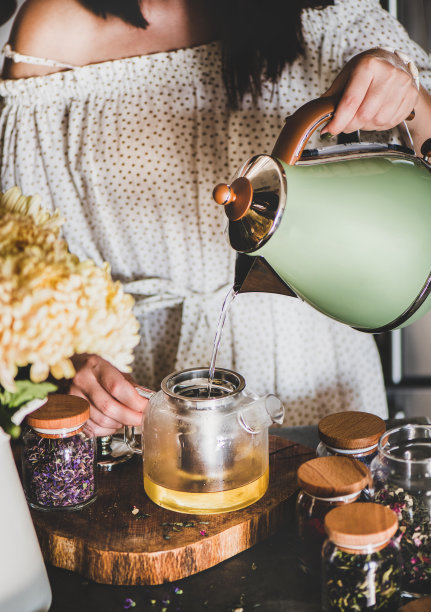 年轻女子在厨房的玻璃壶里泡茶图片下载