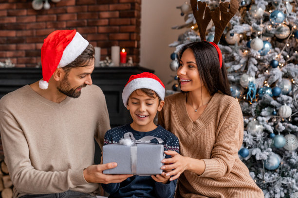 白种人父母和他们戴着圣诞帽的小儿子一起在圣诞树旁度过时光图片下载