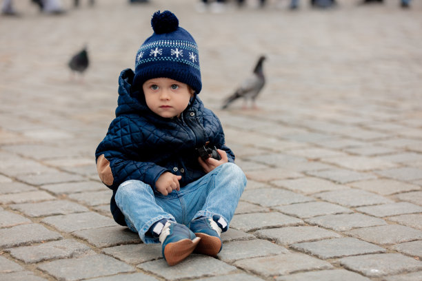 一个蹒跚学步的小男孩坐在城市广场的铺路石上图片下载