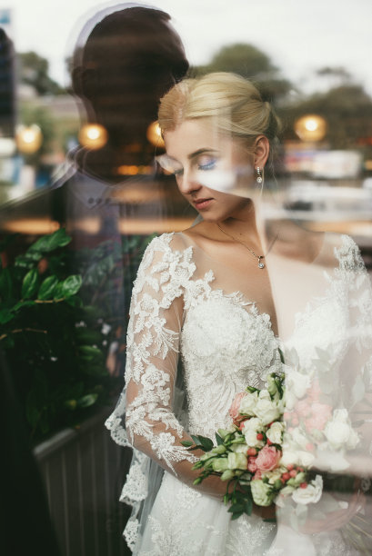 新娘的肖像透过玻璃橱窗与反映剪影的新郎。有创意的婚礼照片。图片下载