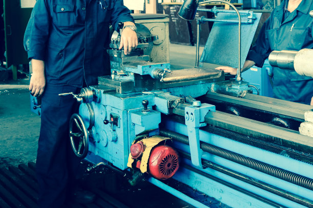 大型金属铁工业车削和螺丝切割机，用于加工金属和零件，备件和一个工人在工厂穿着长袍图片下载
