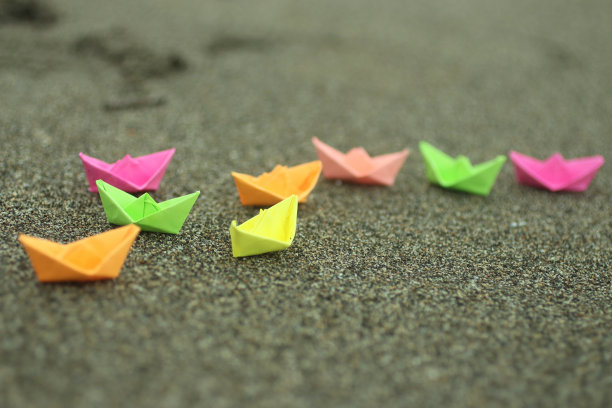 以海沙为背景的彩色纸船。图片下载