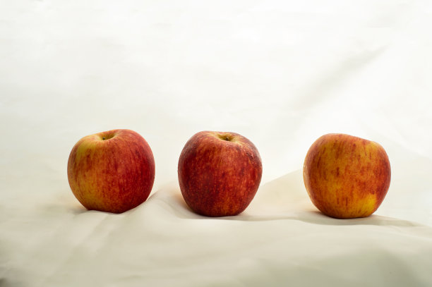 三个红黄苹果水果作为食物的静物，白色米色织物为背景，风格经典图片下载