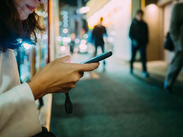 亚洲女人晚上在城市街道上用智能手机发短信。图片下载