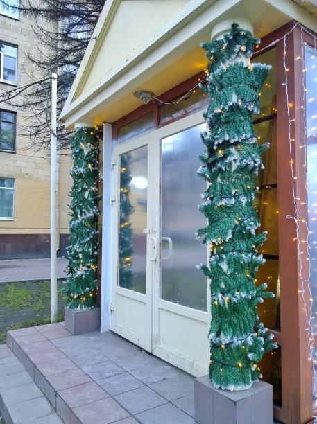 新年装饰街附近的咖啡馆入口。白色的门周围是圣诞树的树枝和缀有小发光灯泡的花环。现代都市的寒假。传统的圣诞装饰。图片下载