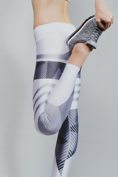 健康的女人。年轻女子在做伸展运动。后视图。穿着白色打底裤和灰色运动鞋。图片下载