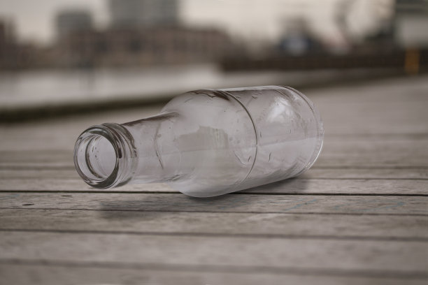 空玻璃瓶躺在木板路上被丢弃。近距离选择焦点图像。图片下载