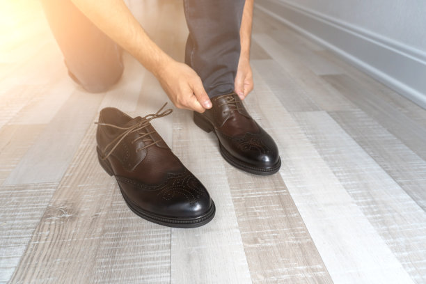 穿着牛仔裤的年轻人坐着，鞋带系在他的棕色鞋子上图片下载